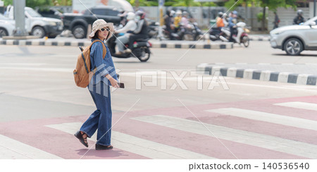 Asian woman tourist crossing urban street with backpack for city exploration and summer travel Asian woman tourist crossing urban street with backpack for city exploration and summer travel 140536540