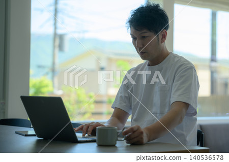 A man working on his laptop, with the view outside the window. 140536578