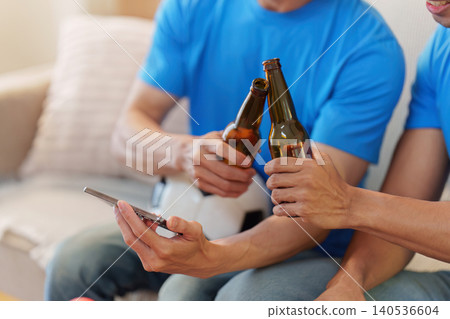 Asian men toasting beer bottles while watching sports at home 140536604