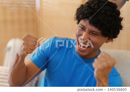 Excited Asian man celebrating victory while watching sports at home Excited Asian man celebrating victory while watching sports at home 140536605