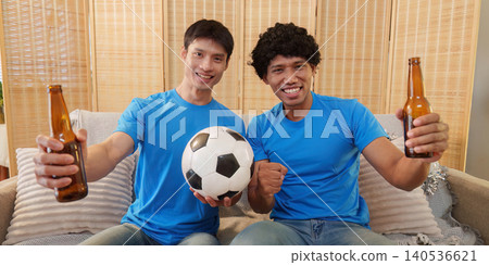 Two happy Asian men holding beer and soccer ball at home 140536621