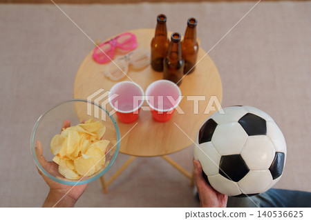 Person holding soccer ball and chips at home for sports fan entertainment Person holding soccer ball and chips at home for sports fan entertainment 140536625