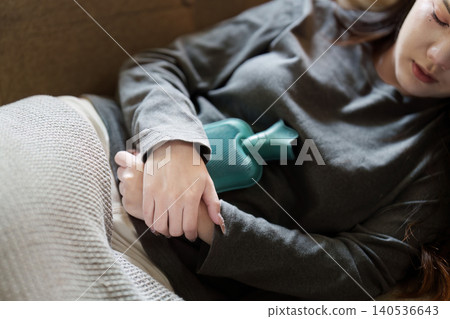 Asian woman using hot water bottle for stomach pain relief at home Asian woman using hot water bottle for stomach pain relief at home 140536643