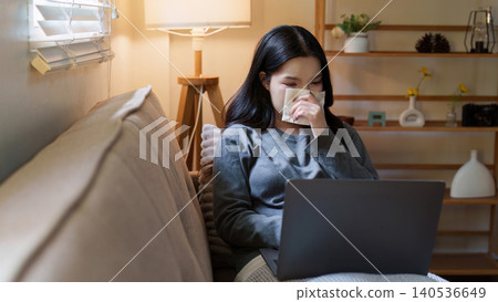Asian woman blowing nose while working on laptop at home for remote work Asian woman blowing nose while working on laptop at home for remote work 140536649