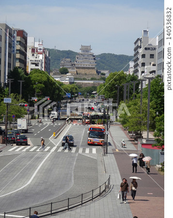 A view from the deck in front of Himeji Station, showing the pedestrian crossing and buses on Otemae Street, with Himeji Castle towering in the distance. 140536832
