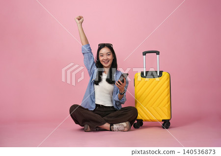 Asian woman celebrating travel booking success with smartphone and luggage Asian woman celebrating travel booking success with smartphone and luggage 140536873