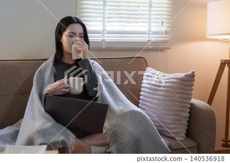 Asian woman blowing nose while working on laptop at home for remote work 140536918