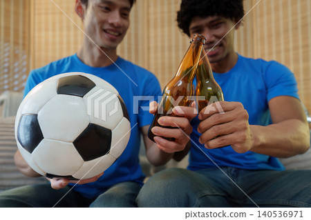Asian and Southeast Asian men toasting beer while watching football 140536971