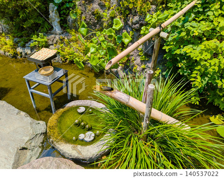 A Japanese garden bathed in early summer sunlight, featuring a deer scarer and a stone water basin. A Japanese garden bathed in early summer sunlight, featuring a deer scarer and a stone water basin. 140537022