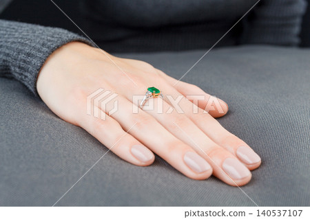 Beautiful female hand with gold ring with diamonds and emerald on gray background Beautiful female hand with gold ring with diamonds and emerald on gray background 140537107