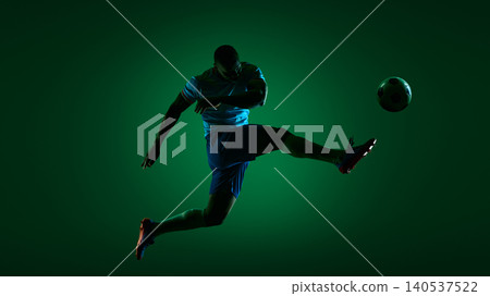 Soccer player kicking ball in dark green studio sport scene. Soccer player kicking ball in dark green studio sport scene. 140537522