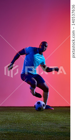 Soccer player dribbling ball in blue uniform on dramatic pink studio field. Soccer player dribbling ball in blue uniform on dramatic pink studio field. 140537636