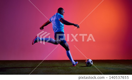 Football player striking ball from behind on grass field with neon studio background Football player striking ball from behind on grass field with neon studio background 140537655