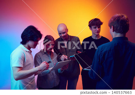 Tech team reviewing tablet and laptop during digital workflow meeting in colorful studio. Tech team reviewing tablet and laptop during digital workflow meeting in colorful studio. 140537663