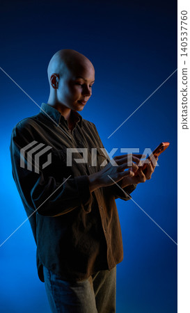 Bald woman using smartphone on blue gradient studio background 140537760