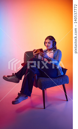 Young woman wearing headphones using smartphone in colorful studio chair scene. 140537772