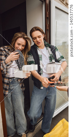 Couple unpacking online delivery boxes and paying courier at apartment entrance. Couple unpacking online delivery boxes and paying courier at apartment entrance. 140537776