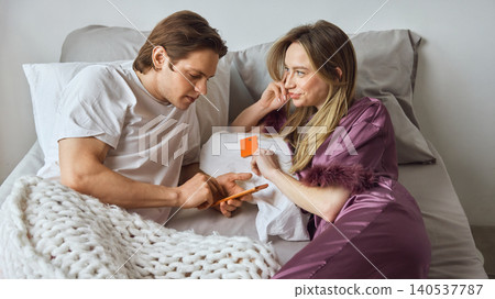 Couple choosing online order with smartphone and payment card in bed. Couple choosing online order with smartphone and payment card in bed. 140537787