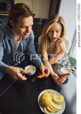 Smiling couple comparing phone and payment card during home online shopping Smiling couple comparing phone and payment card during home online shopping 140537800