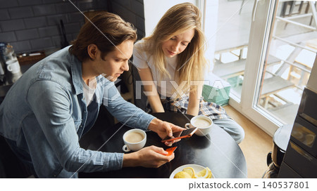 Couple using phone and bank card for online order at kitchen table. Couple using phone and bank card for online order at kitchen table. 140537801