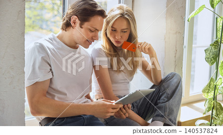 Couple choosing bank card for online purchase on tablet in bright apartment. Couple choosing bank card for online purchase on tablet in bright apartment. 140537824