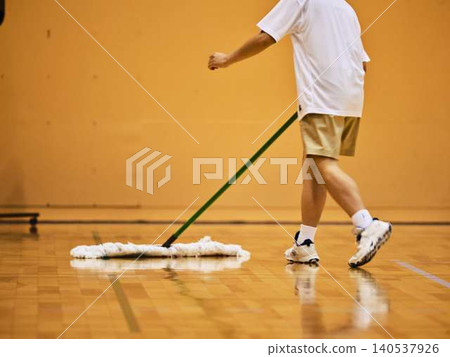 A Japanese man in sportswear mops a gymnasium. A Japanese man in sportswear mops a gymnasium. 140537926