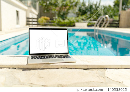 Laptop with blank white screen on a swimming pool edge 140538025