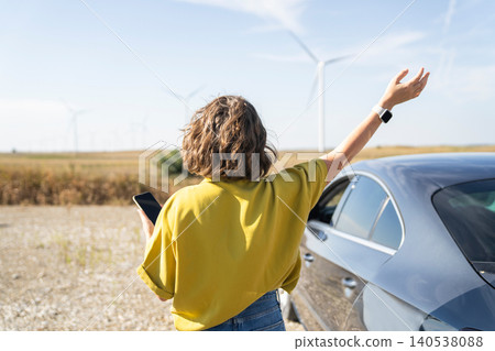 Woman using smartphone near car looking at wind farm on the horizon 140538088