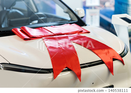 Big red gift bow on the hood of a new car in showroom Big red gift bow on the hood of a new car in showroom 140538111