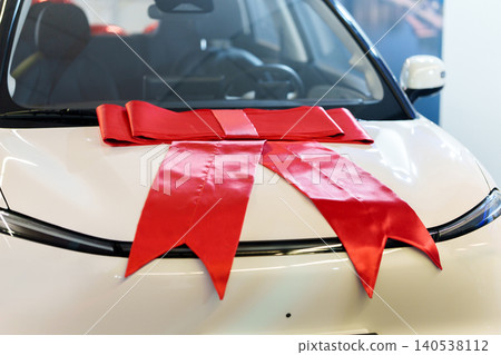 Big red gift bow on the hood of a new car in showroom Big red gift bow on the hood of a new car in showroom 140538112