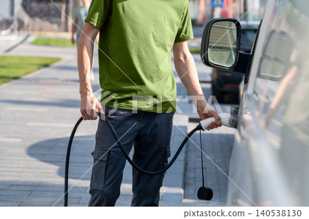 Driver with charging plug next to of electric van. Driver with charging plug next to of electric van. 140538130