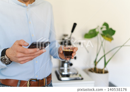 Man taking a break with espresso and smartphone, manual coffee maker in the background Man taking a break with espresso and smartphone, manual coffee maker in the background 140538176