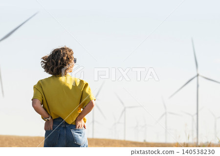 Rear view of a woman observing wind turbines in the countryside Rear view of a woman observing wind turbines in the countryside 140538230