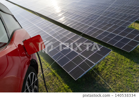 Close up of electric car with a connected charging cable on the background of solar panels.. Close up of electric car with a connected charging cable on the background of solar panels.. 140538334