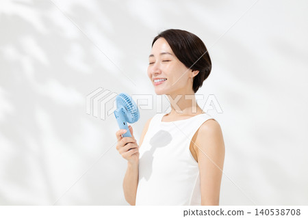 A woman cooling herself with a handheld fan. 140538708
