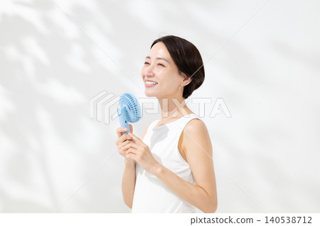 A woman cooling herself with a handheld fan. A woman cooling herself with a handheld fan. 140538712