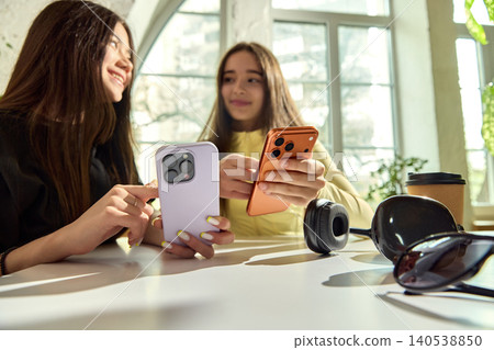 Teenage girls transferring money with smartphones at bright table. Teenage girls transferring money with smartphones at bright table. 140538850
