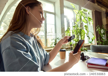 Woman transferring money by smartphone with bank card at sunny table. Woman transferring money by smartphone with bank card at sunny table. 140538863