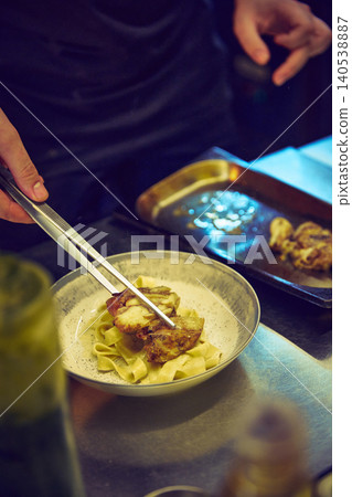 Chef placing grilled chicken on creamy pasta in restaurant kitchen. Chef placing grilled chicken on creamy pasta in restaurant kitchen. 140538887