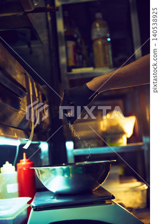 Chef sprinkling seasoning into metal mixing bowl on restaurant kitchen scale. Chef sprinkling seasoning into metal mixing bowl on restaurant kitchen scale. 140538925