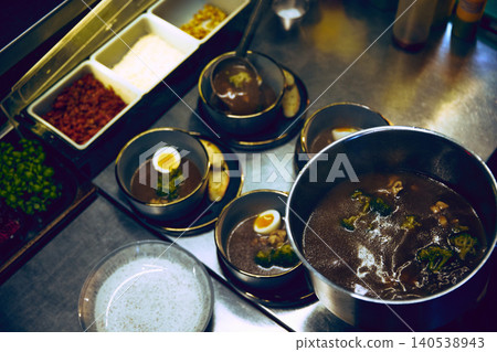 Chef plating dark soup bowls with egg garnish on stainless kitchen counter. Chef plating dark soup bowls with egg garnish on stainless kitchen counter. 140538943