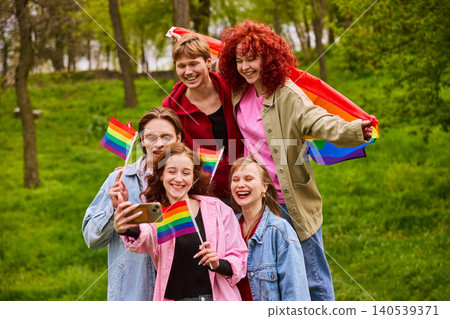 Young friends taking selfie with rainbow flags at pride picnic in park 140539371