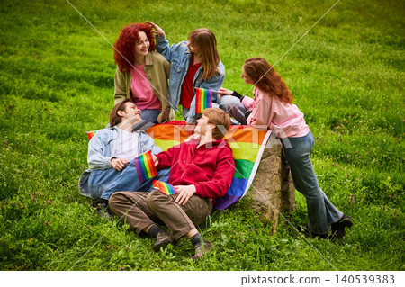 Happy young friends relaxing with rainbow flags on grass in park. 140539383