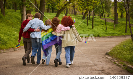 Group of young friends walking away with rainbow flag in green park. 140539387