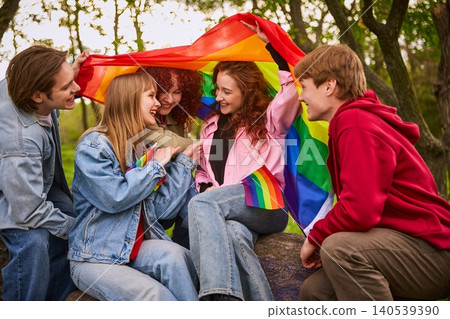 Happy young friends laughing under rainbow flag in summer park. 140539390
