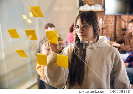 Focused woman writing ideas on sticky notes during team workshop. Focused woman writing ideas on sticky notes during team workshop. 140539528