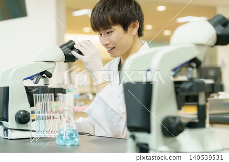 一位身穿白色實驗服的日本青年正在使用顯微鏡進行實驗、研究、開發和學習。 一位身穿白色實驗服的日本青年正在使用顯微鏡進行實驗、研究、開發和學習。 140539531