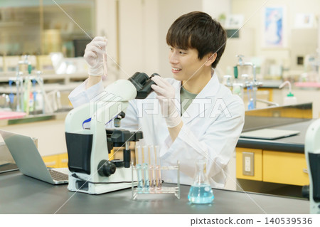 一位身穿白色實驗服的日本青年正在使用顯微鏡進行實驗、研究、開發和學習。 140539536