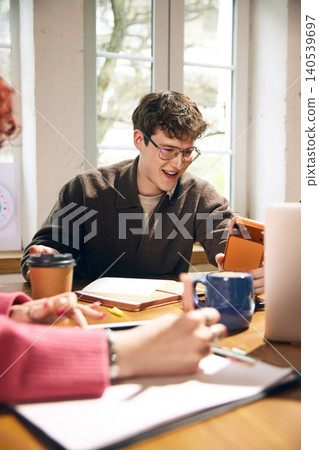 Young office worker smiling with smartphone during creative team meeting. Young office worker smiling with smartphone during creative team meeting. 140539697