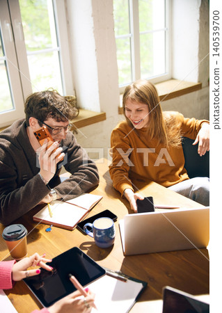 Young coworkers laughing and planning project together near sunny windows. Young coworkers laughing and planning project together near sunny windows. 140539700